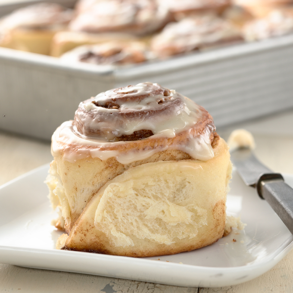 single glazed cinnamon bun in front of pan of rolls