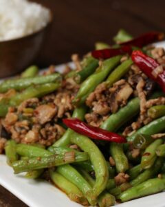 fresh green beans and crumbled cooked pork sausage with hot peppers in pan