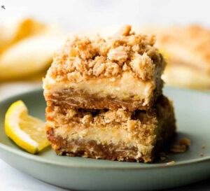 two lemon crumblebar cookies on a green plate with slice of lemon on the side